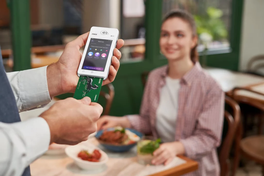 Un client règle son addition dans un restaurant en insérant sa carte bancaire dans un terminal de paiement A50, offrant une solution de paiement rapide et sécurisée